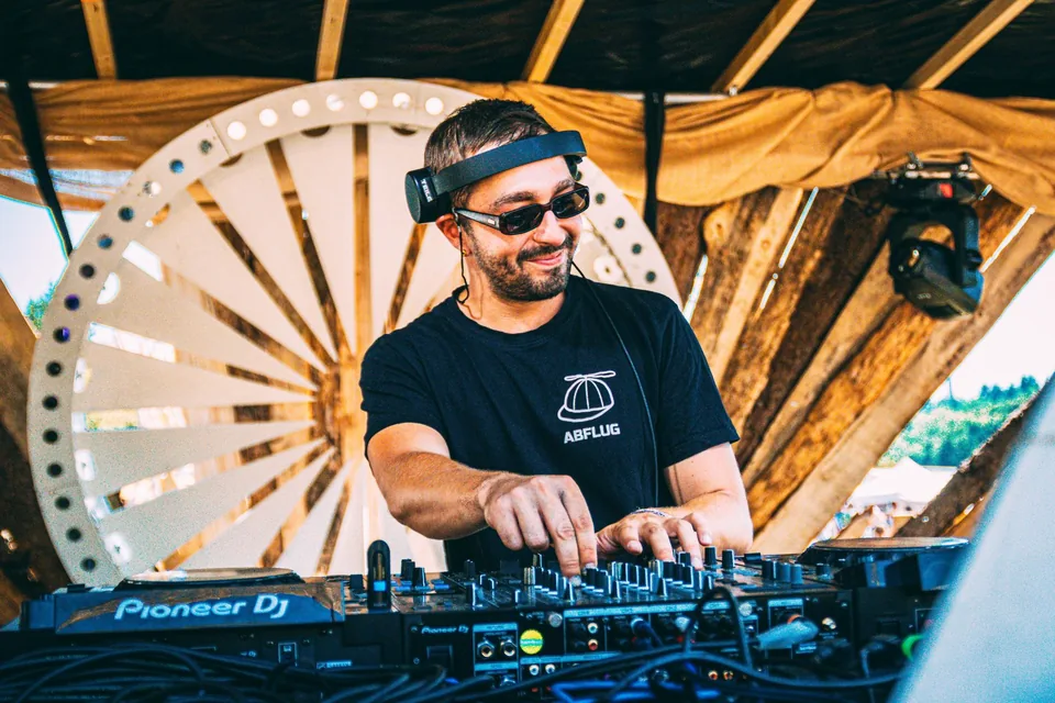 DJ lacht am Pult bei Tageslicht